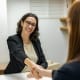 a woman shaking hands with another woman sitting at a table