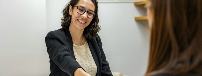 a woman shaking hands with another woman sitting at a table