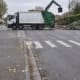 Un camion de collecte des déchets manœuvre à un croisement, avec des sacs de déchets en désordre sur le bord de la route dans un quartier résidentiel