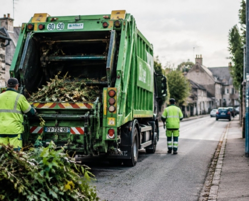 Photo réaliste d'un camion de collecte des déchets verts en action, chargé de branches et feuillage, sur une rue de Bénouville